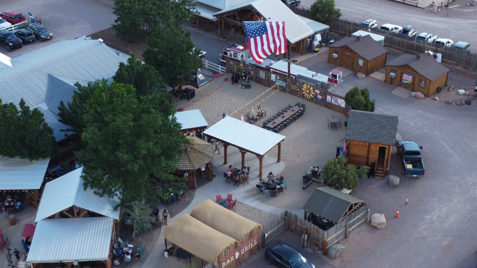 American flag flanked by timber pavilion structure, warm string lights, and the live music stage — classic WWBG July 4th ambiance.