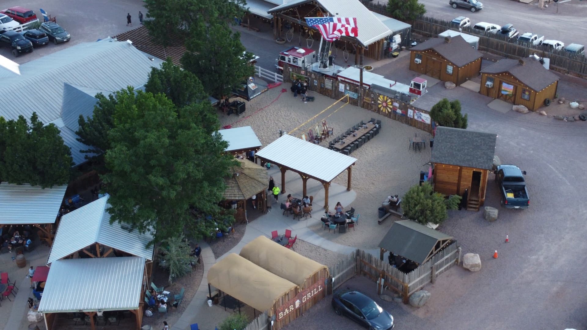 Close-up aerial of the timber dining pavilion with guests seated, string lights overhead, and the rustic western atmosphere of WWBG in full swing.